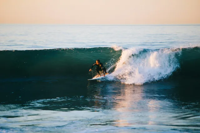 Surfer walking into waves on a Welsh beach at sunset
